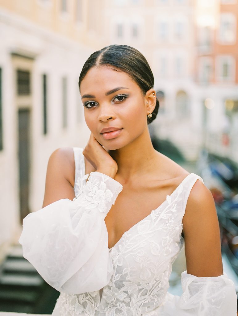 A portrait of a bride in Venice Italy on a bridge over one of the Venice canals, the bride is wearing a lace wedding dress with sleeves, it is a close up of the bride after eloping image photographed by Kelley Williams Photography a Venice Italy wedding photographer. 