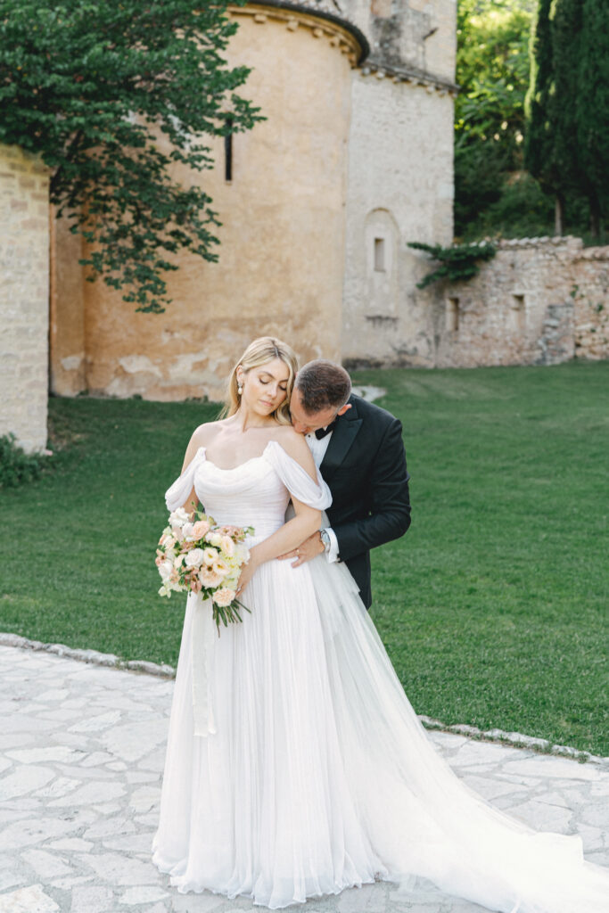 Groom kissing the bride's shoulder, Abbazia San Pietro in Valle wedding, image taken by Kelley Williams a wedding photographer in Umbria Italy